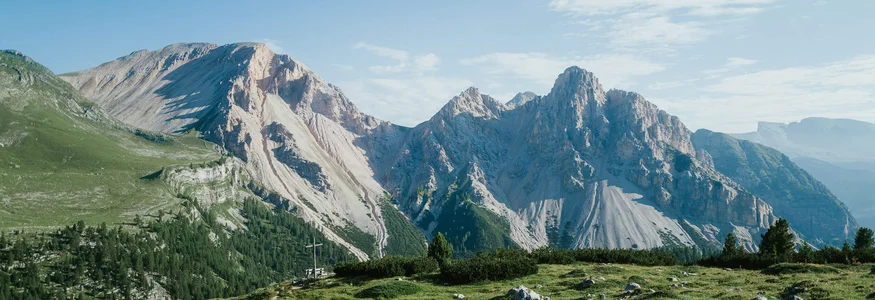 Grüne Wiese mit Felsen vor steilen Bergen unter blauem Himmel