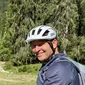 Mann mit Helm auf Fahrrad in grüner Alpenseenlandschaft mit Kühen