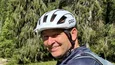 Mann mit Helm auf Fahrrad in grüner Alpenseenlandschaft mit Kühen