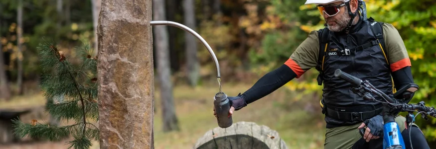 Radfahrer füllt Wasserflasche an Brunnen im Wald