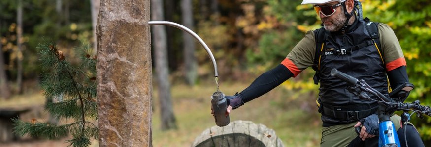 Radfahrer füllt Wasserflasche an Brunnen im Wald