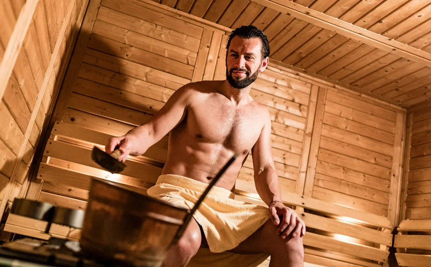 Man in towel sitting in sauna pouring water on stove