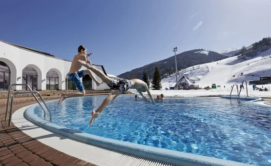 Sonnenskilauf & Therme im März / 5 Nächte Kinderen springen in een buitenzwembad met besneeuwde bergen op de achtergrond