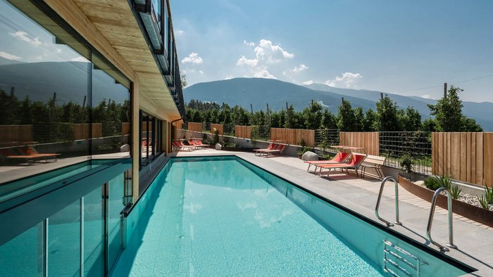 Moderner Außenpool neben Gebäude mit Liegestühlen vor Bergkulisse