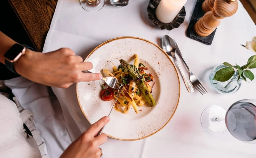 Person eating pasta with asparagus and tomatoes at a set table