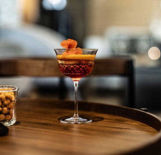 Cocktail glass with red drink, orange peel, and flower on wooden table