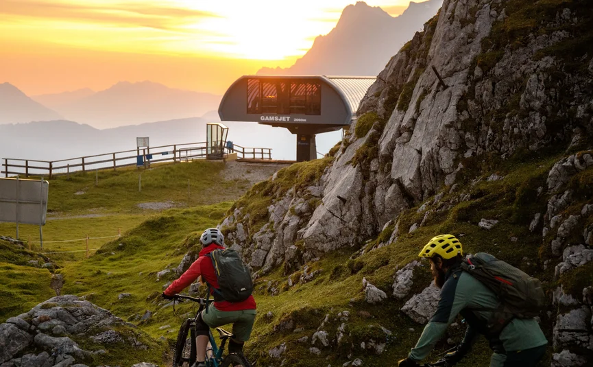 Zwei Mountainbiker fahren bei Sonnenuntergang an einer Bergstation vorbei