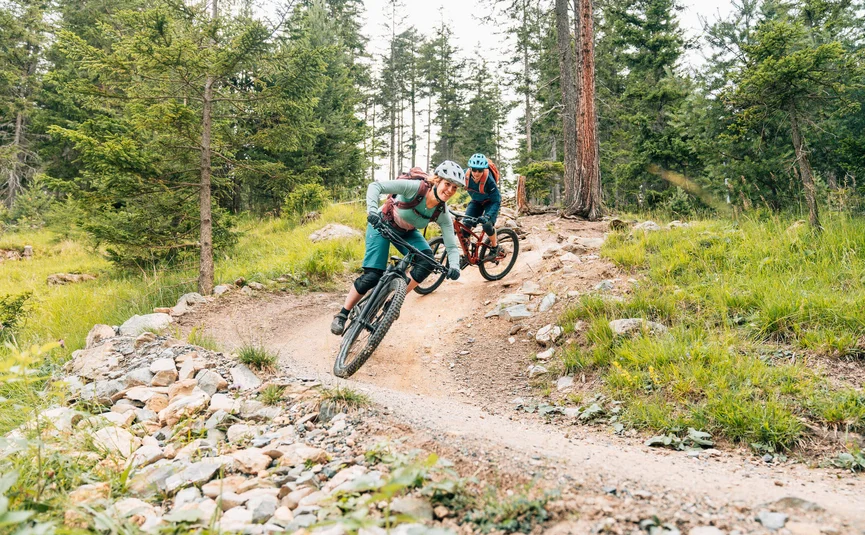 Two mountain bikers ride downhill on a forest trail