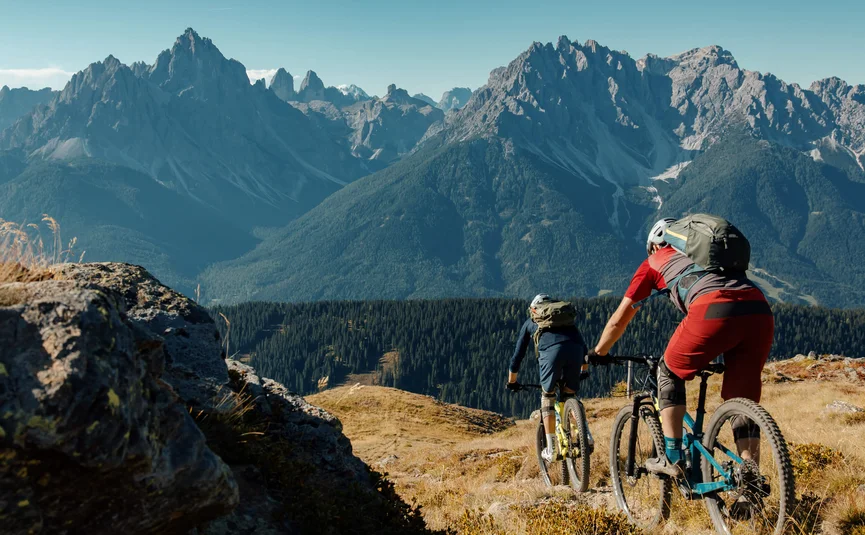 Twee mountainbikers fietsen op een bergpad met Alpen op de achtergrond