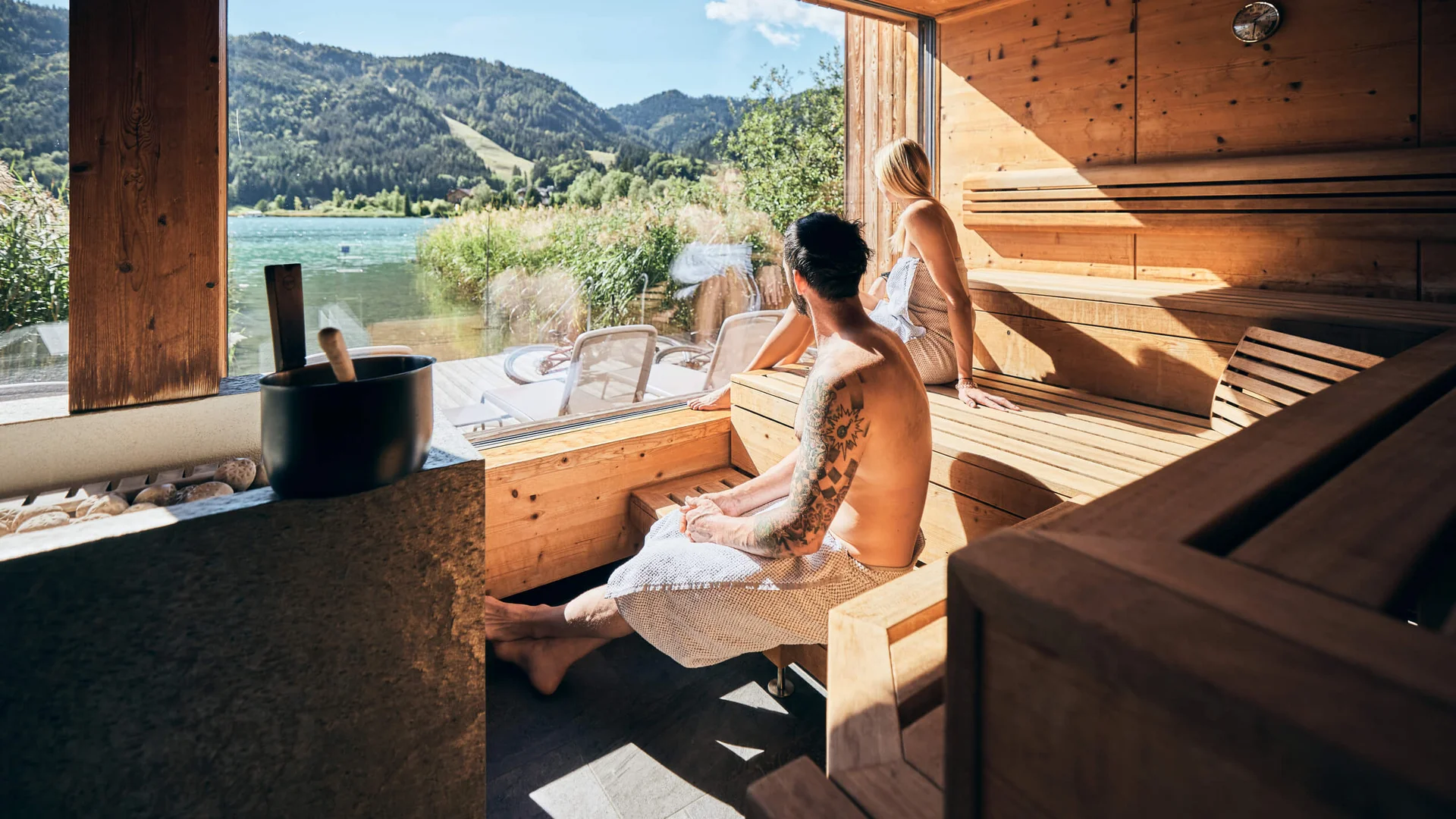 Good to know: 9 Wellness-Funfacts © Tobias Köhler Paar in Sauna mit Blick auf See und Berge durch großes Fenster
