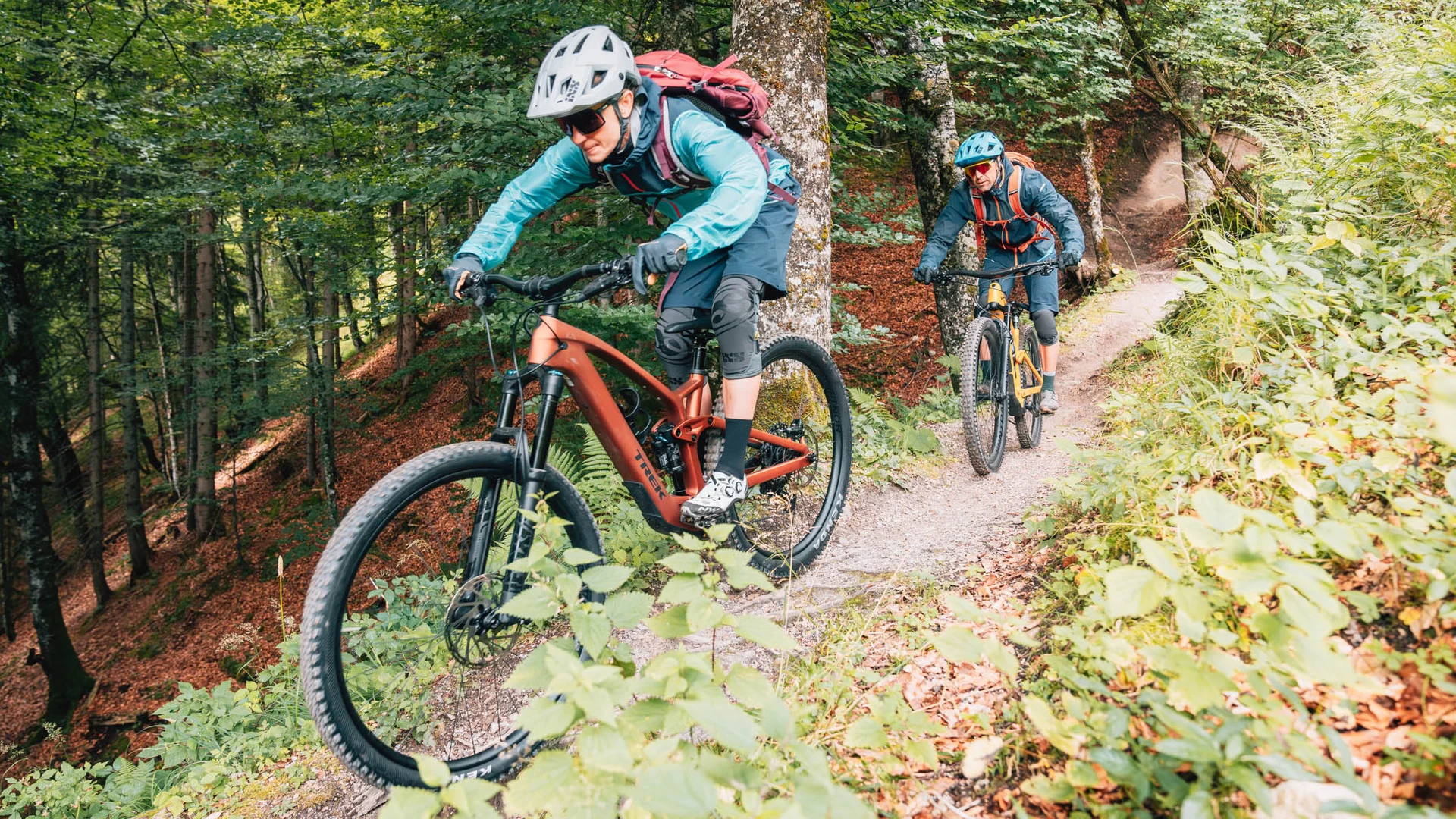 Zwei Personen mountainbiken auf einem Waldweg mit Helm und Schutzausrüstung