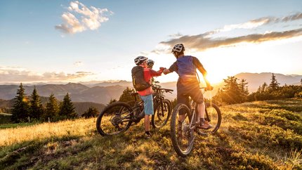 Zwei Mountainbiker grüßen sich bei Sonnenuntergang in den Bergen
