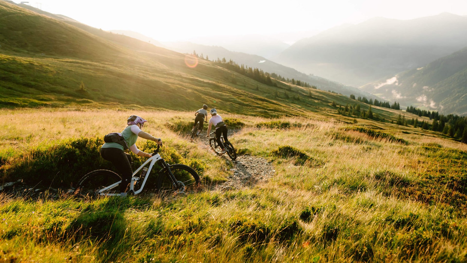 Drei Radfahrer fahren auf einem Bergpfad im Sonnenlicht