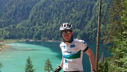 Radfahrer steht mit Mountainbike vor einem See und bewaldeten Bergen