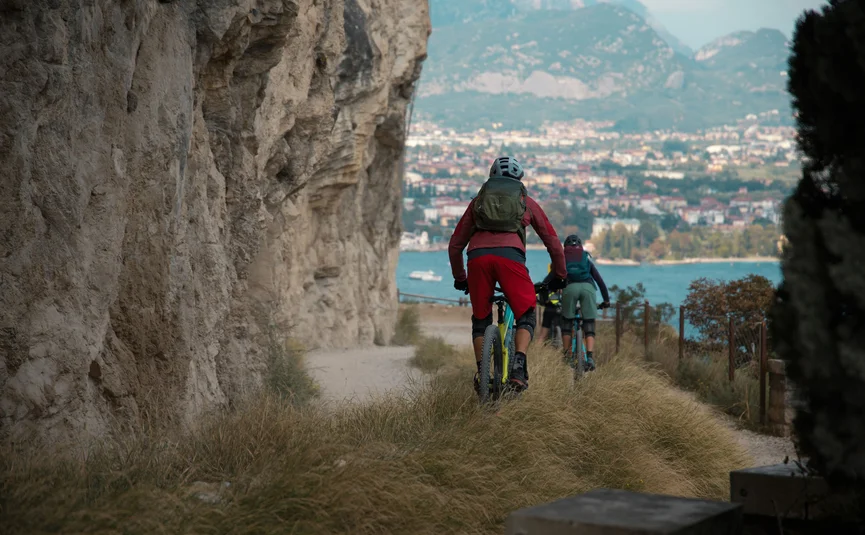 Zwei Mountainbiker fahren an einem Felsen entlang mit Blick auf eine Stadt und Berge