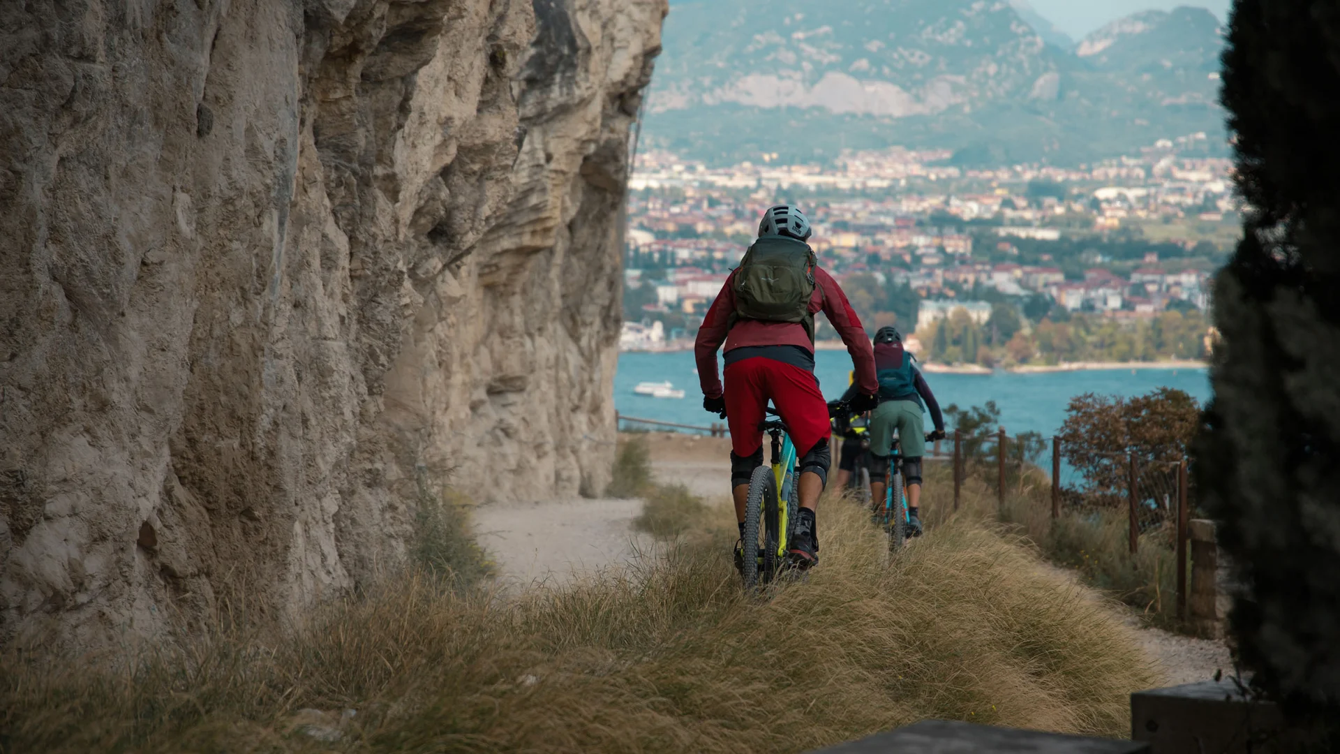Zwei Mountainbiker fahren an einem Felsen entlang mit Blick auf eine Stadt und Berge