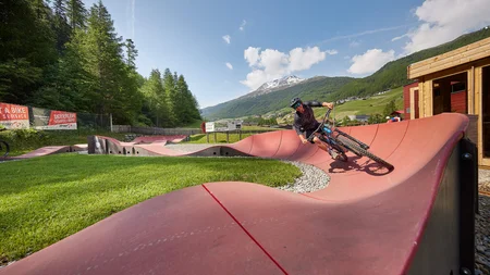 Fahrradfahrer fährt helmbekleidet auf gewellter roten Strecke im Bergtal