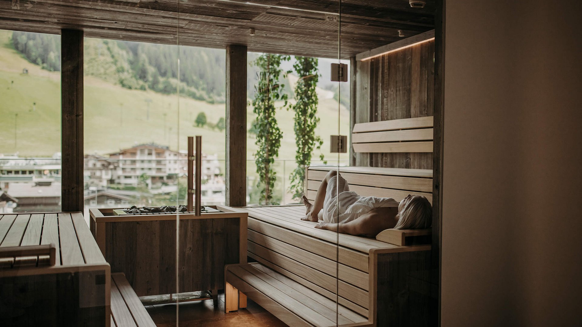 Frau entspannt in moderner Sauna mit Panoramablick auf Berge