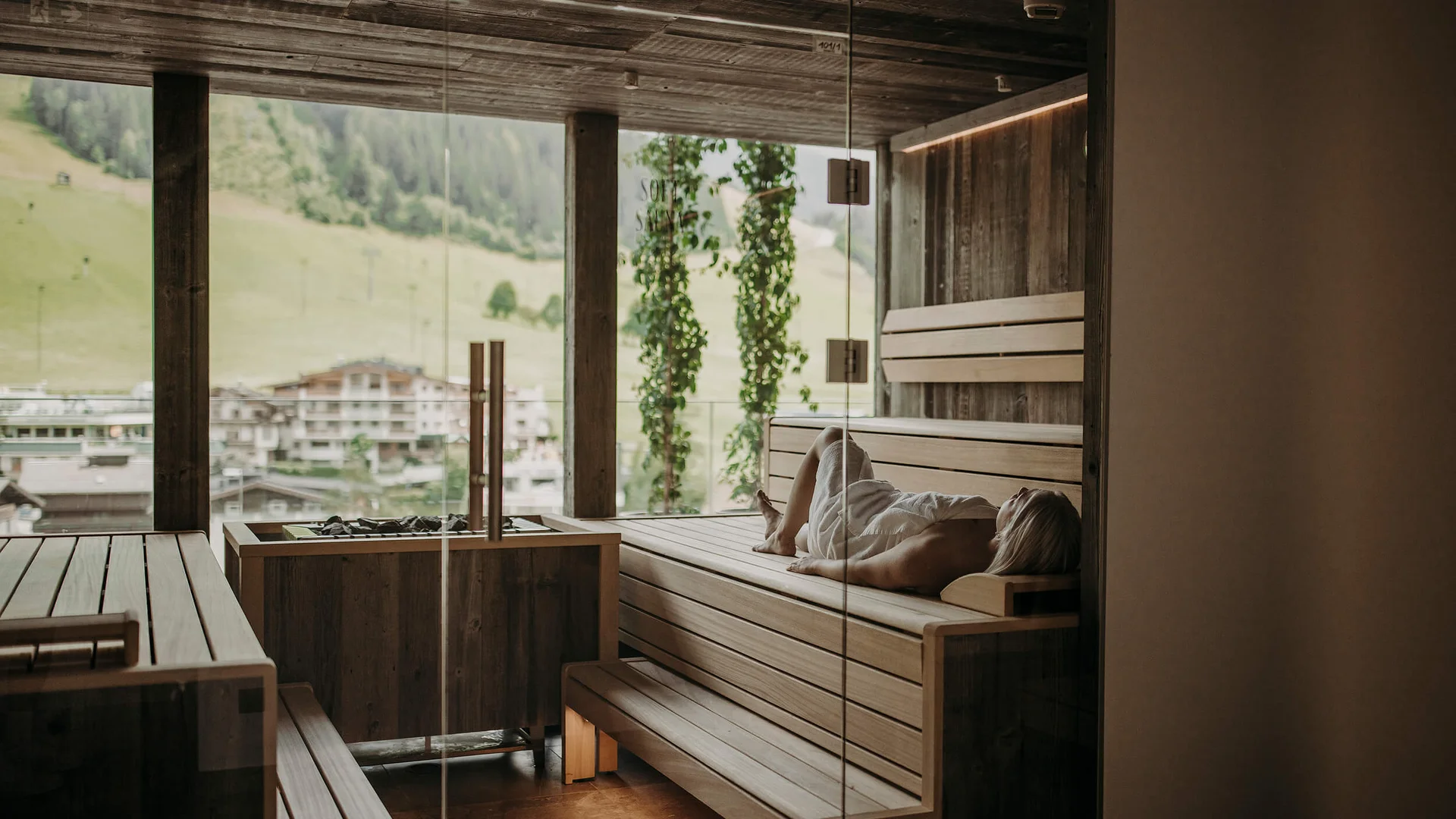 Frau entspannt in moderner Sauna mit Panoramablick auf Berge