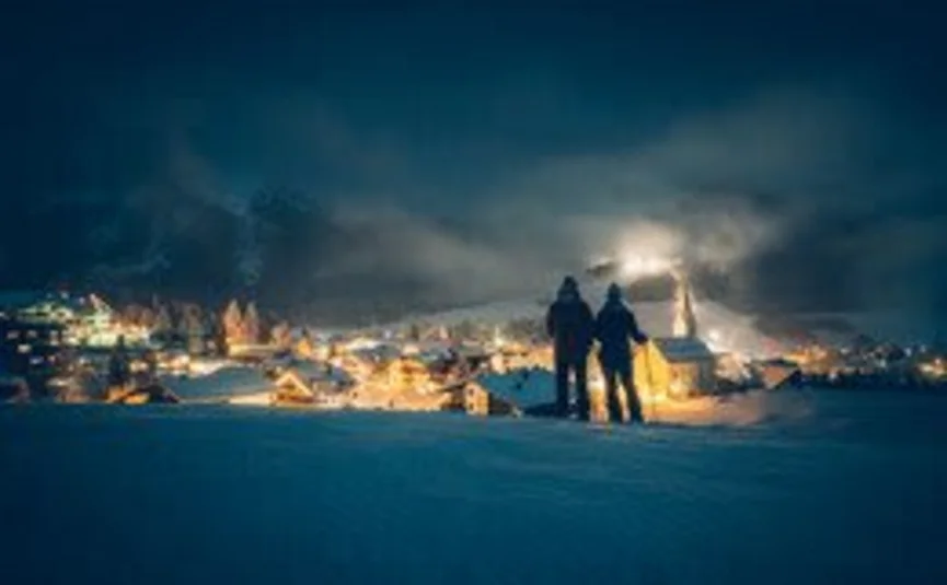 4 Tage Genuss-Skifahren auf der Sonnenseite der Zugspitze 2026-7 Zwei Menschen blicken nachts auf ein beleuchtetes Dorf im Winter