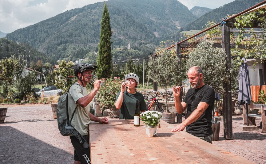 Drei Radfahrer trinken Wein im Freien vor Berglandschaft