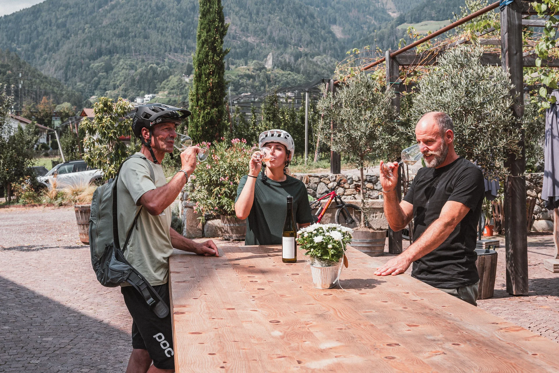 Drei Radfahrer trinken Wein im Freien vor Berglandschaft