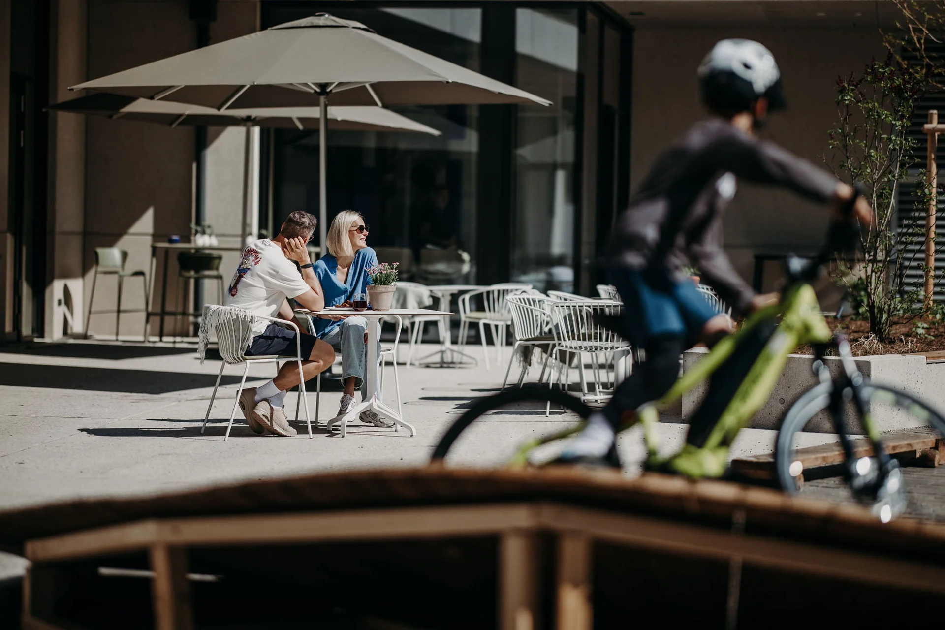 Paar sitzt draußen unter Sonnenschirmen, Radfahrer fährt vorbei
