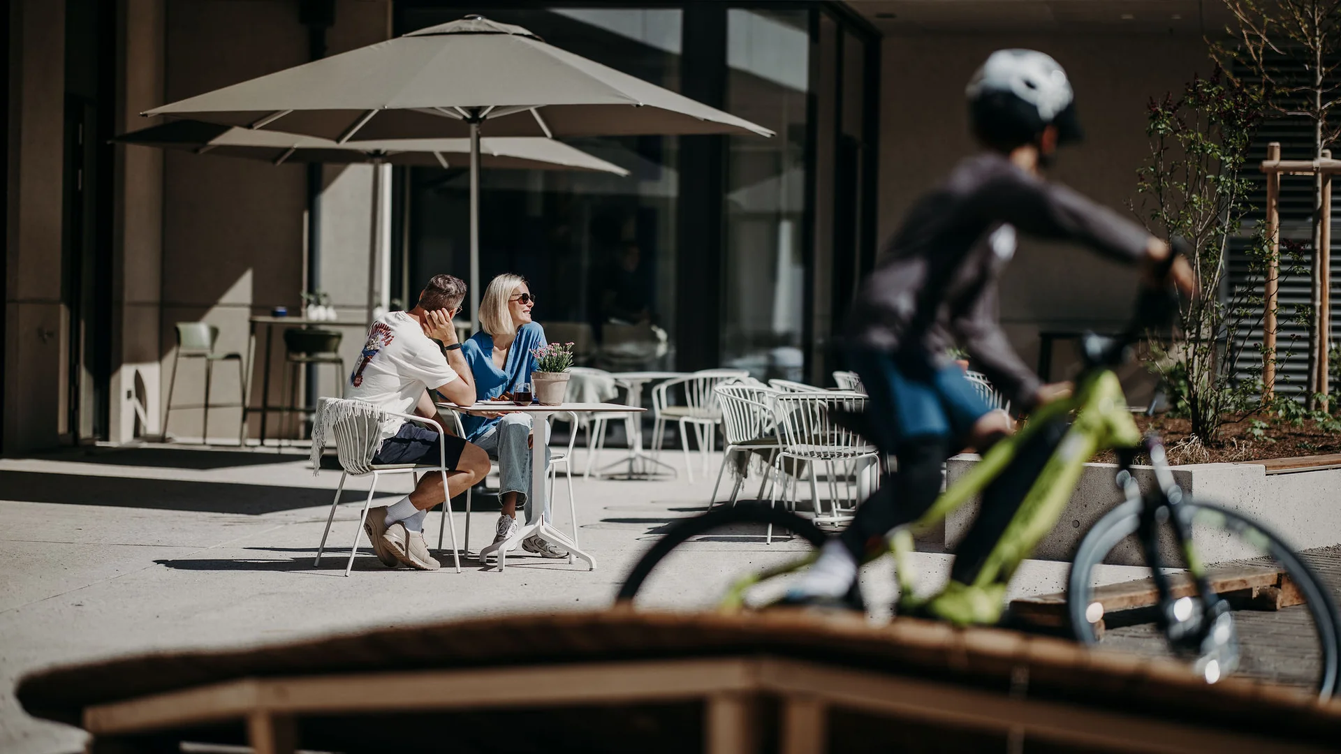 Paar sitzt draußen unter Sonnenschirmen, Radfahrer fährt vorbei