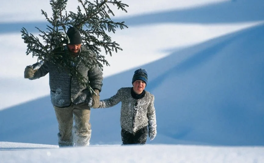 Man en jongen dragen een kerstboom door diepe sneeuw
