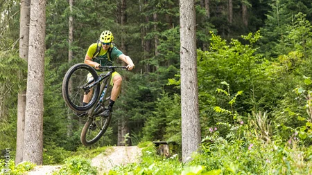 Mountain biker jumping with helmet and glasses on forest trail