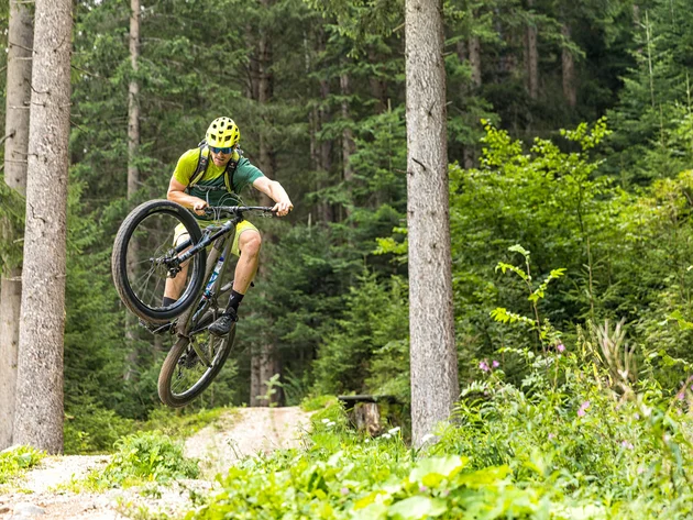Mountain biker jumping with helmet and glasses on forest trail