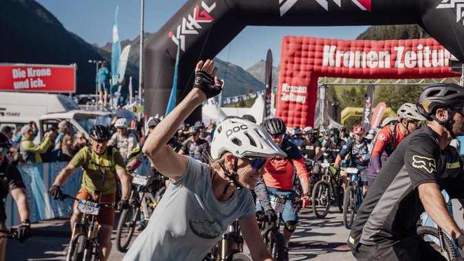 Fahrradfahrer starten bei einem Radrennen unter einem Ischgl-Bogen bei Sonnenschein