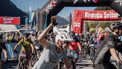 Fahrradfahrer starten bei einem Radrennen unter einem Ischgl-Bogen bei Sonnenschein