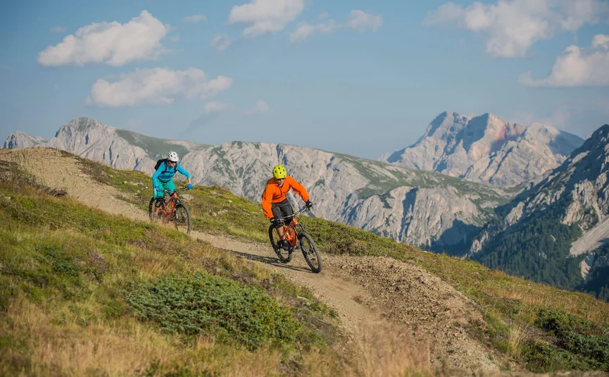Zwei Mountainbiker fahren auf einem Bergweg mit Bergen im Hintergrund
