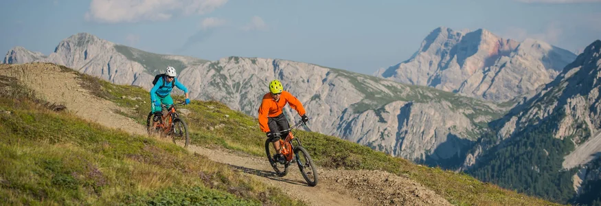 Zwei Mountainbiker fahren auf einem Bergweg mit Bergen im Hintergrund