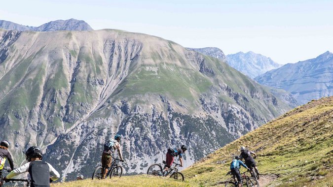 Gruppe Mountainbiker fährt auf Bergpfad mit Alpen im Hintergrund
