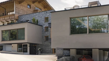 Modernes Hotel mit Kombination aus Holz- und Stein Fassade und rotem Auto vor der Garage