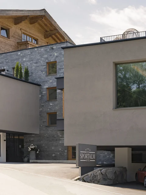 Modernes Hotel mit Kombination aus Holz- und Stein Fassade und rotem Auto vor der Garage
