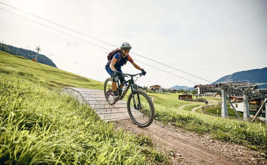 Vrouw mountainbiken op pad met groene heuvels en skilift op de achtergrond