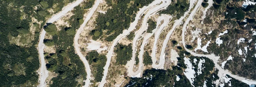Unterwegs auf der Bond-Straße © Tobias Köhler Luftaufnahme einer geschwungenen Bergstraße mit Vegetation und Schneeflecken