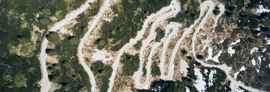 Luftaufnahme einer geschwungenen Bergstraße mit Vegetation und Schneeflecken