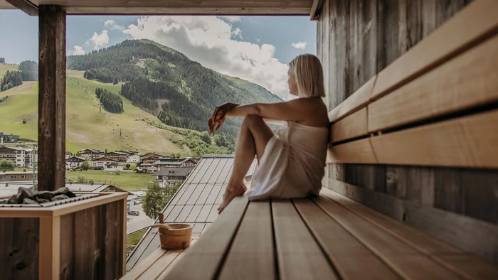 Frau entspannt in Sauna mit Blick auf Berglandschaft und Dorf