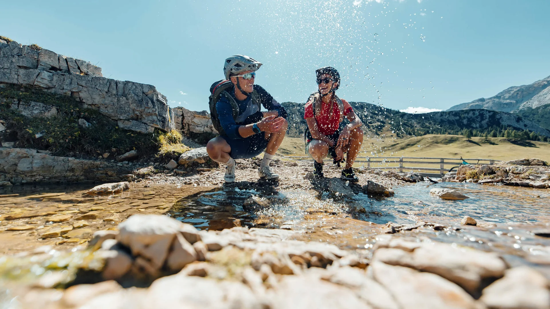 Spätsommer- & Herbstbiken in Toblach © David Karg Zwei Radfahrer entspannen an einem Bergbach und spritzen Wasser