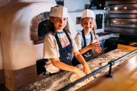 Twee meisjes kneden deeg in een traditionele keuken met houtoven