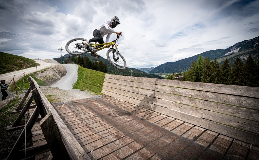 Mountainbiker springt auf Holzrampe in den Bergen bei bewölktem Himmel