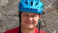 Mann mit blauem Fahrradhelm und rotem T-Shirt vor Steinwand