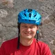 Mann mit blauem Fahrradhelm und rotem T-Shirt vor Steinwand