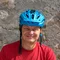 Mann mit blauem Fahrradhelm und rotem T-Shirt vor Steinwand