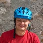 Mann mit blauem Fahrradhelm und rotem T-Shirt vor Steinwand