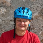 Mann mit blauem Fahrradhelm und rotem T-Shirt vor Steinwand